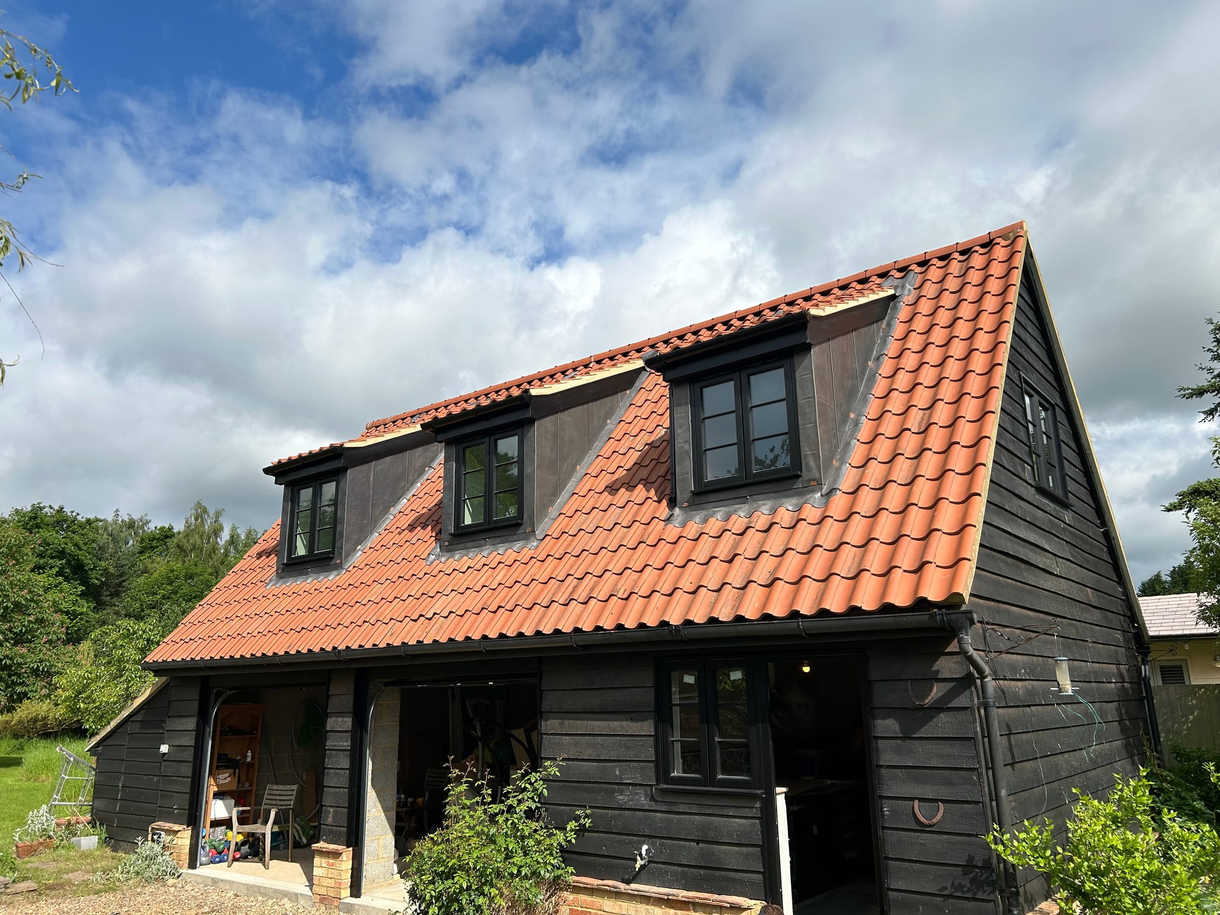 A new black weatherboarded building with a clay tiled roof and dormers