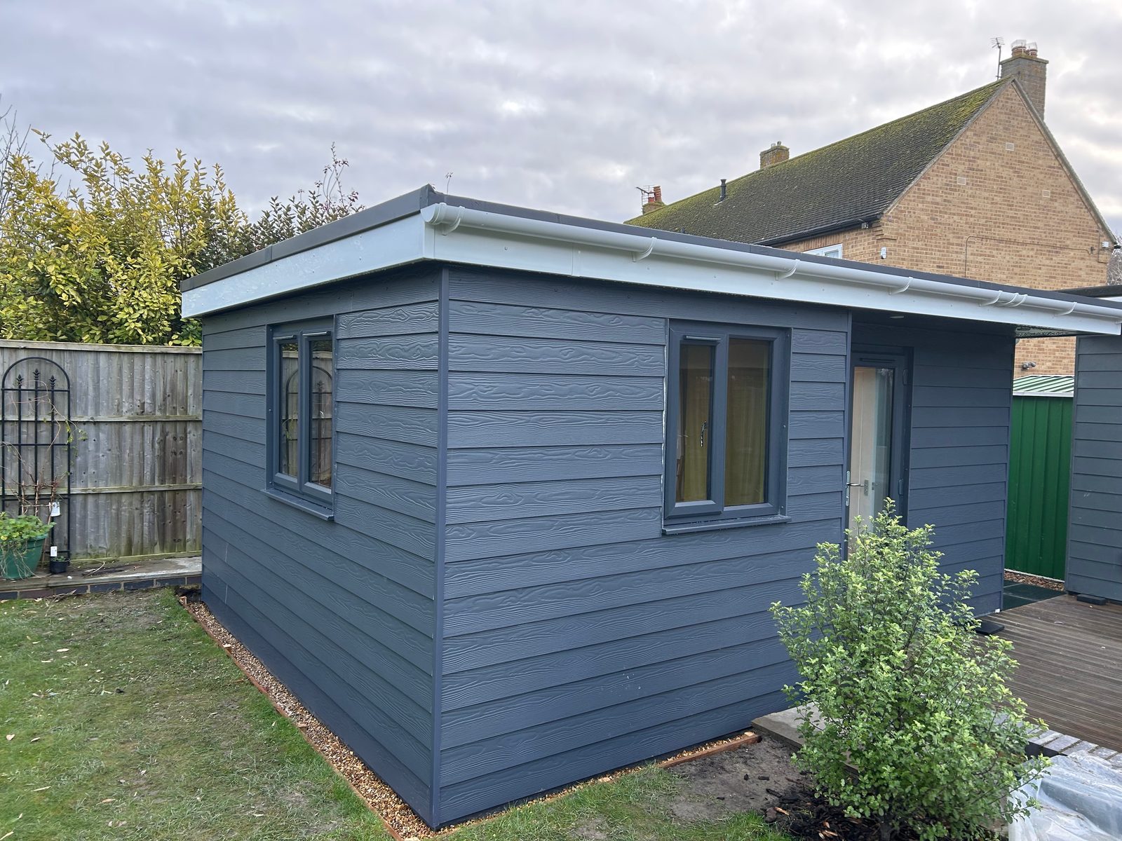 A grey clad garden room on the lawn, with two windows along its side