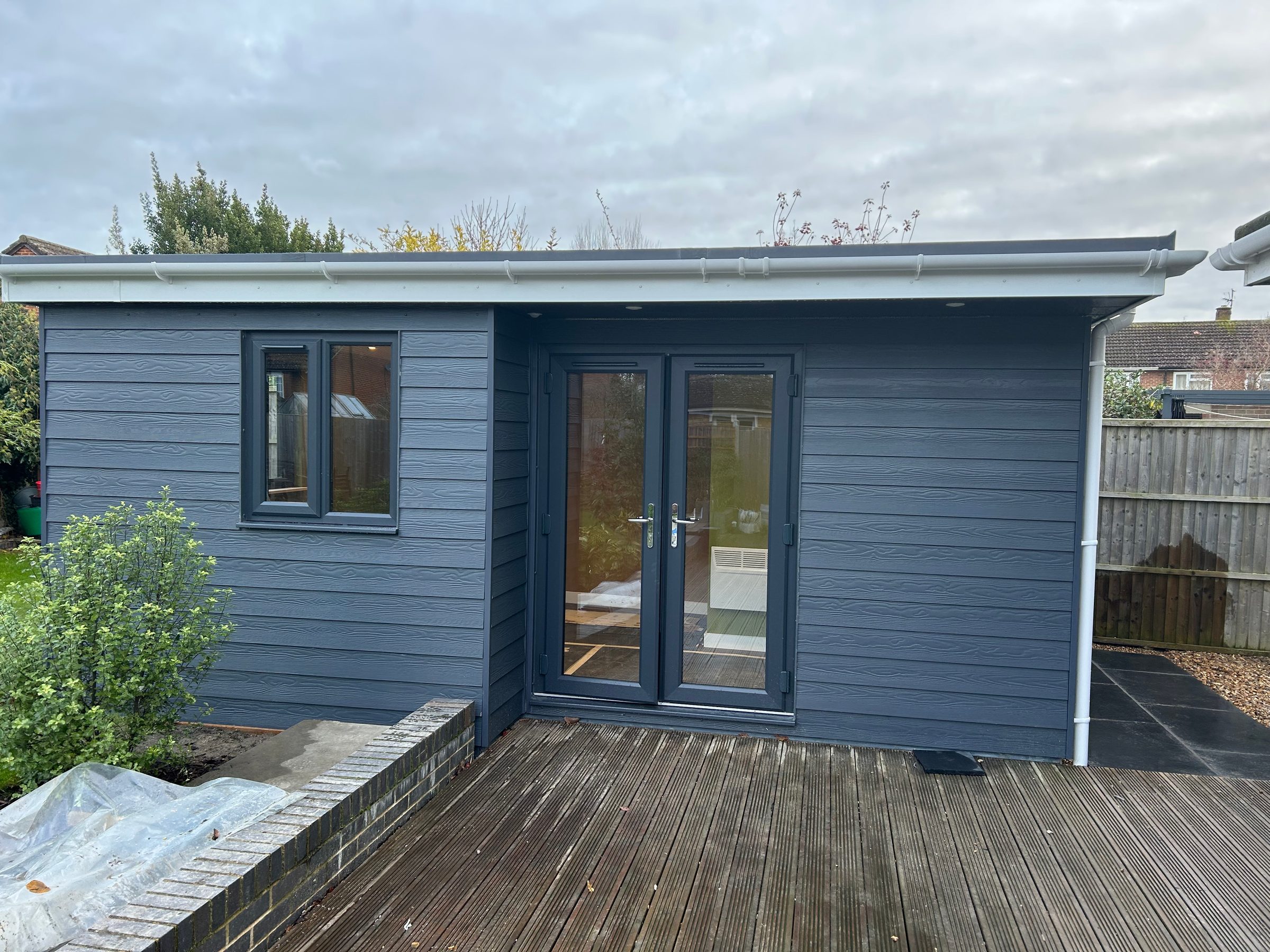 A finished garden room clad in grey boards, with French doors onto decking