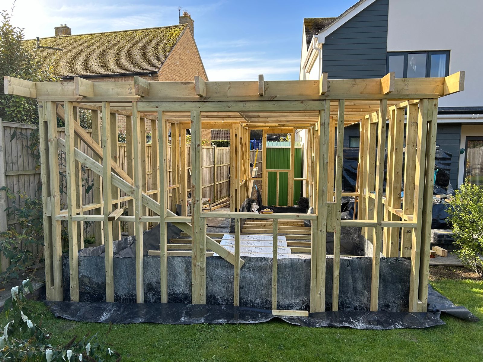 A garden room's timber frame going up on its raised base, on the lawn