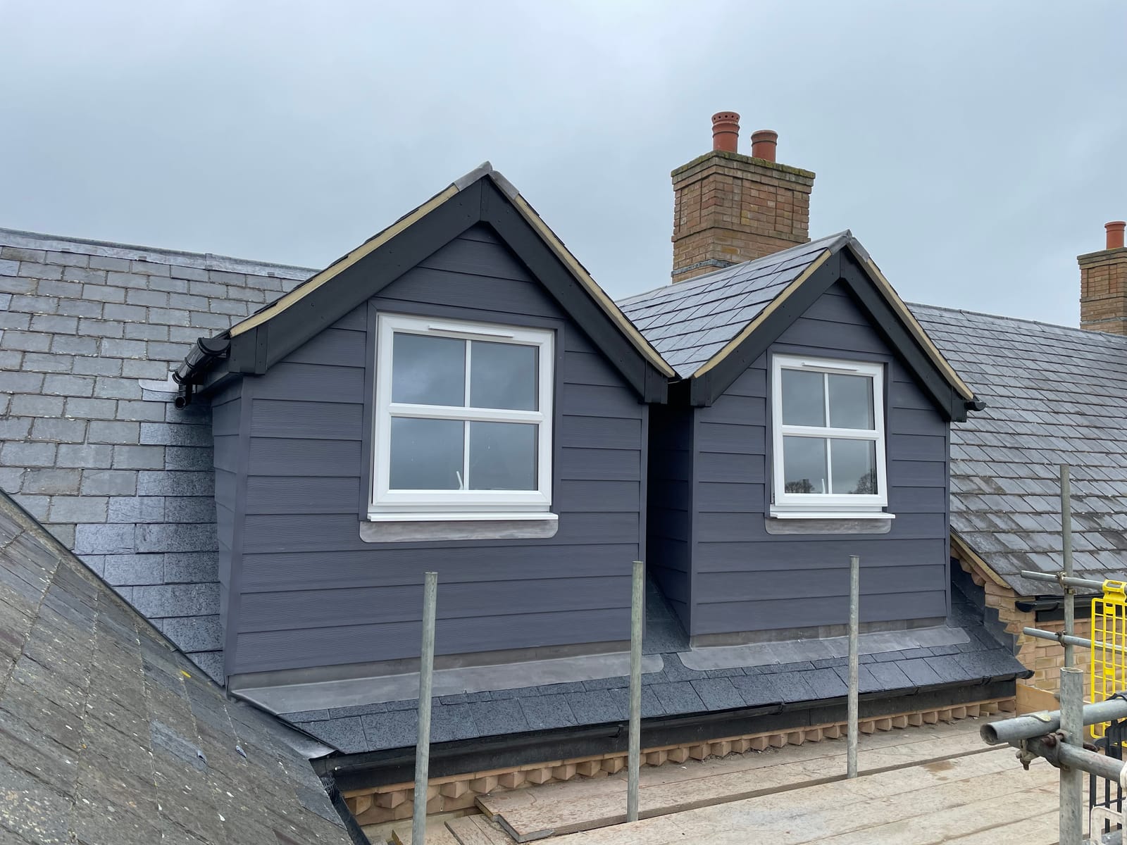 Two finished dormers clad in dark grey on a slate roof